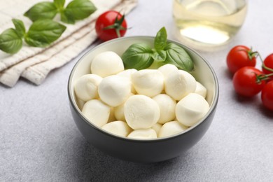 Photo of Tasty mozzarella cheese balls, tomatoes and basil on light grey table, closeup