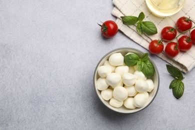 Photo of Tasty mozzarella cheese balls, tomatoes and basil on light grey table, flat lay. Space for text