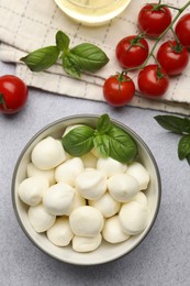 Photo of Tasty mozzarella cheese balls, tomatoes and basil on light grey table, flat lay