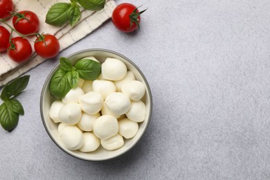 Photo of Tasty mozzarella cheese balls, tomatoes and basil on light grey table, flat lay. Space for text