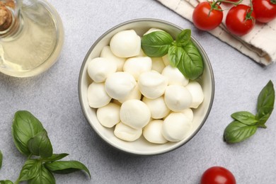 Photo of Tasty mozzarella cheese balls, tomatoes and basil on light grey table, flat lay