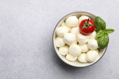 Photo of Tasty mozzarella cheese balls, tomato and basil on light grey table, top view. Space for text