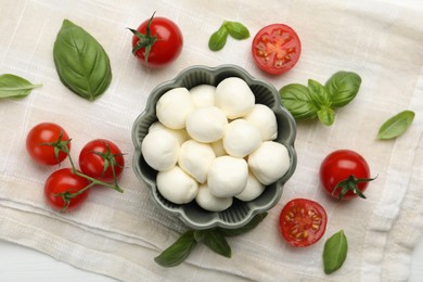 Photo of Tasty mozzarella cheese balls, tomatoes and basil on white wooden table, flat lay