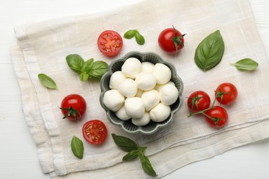 Photo of Tasty mozzarella cheese balls, tomatoes and basil on white wooden table, flat lay