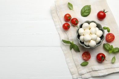 Photo of Tasty mozzarella cheese balls, tomatoes and basil on white wooden table, flat lay. Space for text