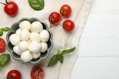 Photo of Tasty mozzarella cheese balls, tomatoes and basil on white wooden table, flat lay. Space for text