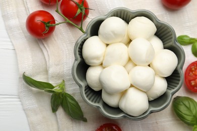 Photo of Tasty mozzarella cheese balls, tomatoes and basil on white wooden table, flat lay