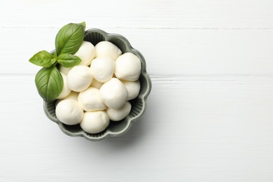 Photo of Tasty mozzarella cheese balls and basil on white wooden table, top view. Space for text