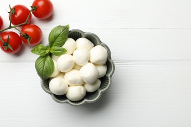 Photo of Tasty mozzarella cheese balls, tomatoes and basil on white wooden table, flat lay. Space for text