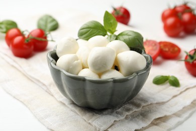 Photo of Tasty mozzarella cheese balls, tomatoes and basil on white wooden table, closeup