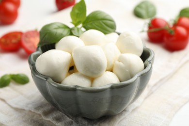 Photo of Tasty mozzarella cheese balls, tomatoes and basil on white wooden table, closeup