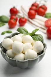 Photo of Tasty mozzarella cheese balls, tomatoes and basil on white wooden table, closeup