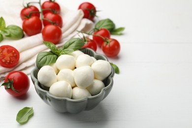 Photo of Tasty mozzarella cheese balls, tomatoes and basil on white wooden table, closeup. Space for text