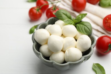 Photo of Tasty mozzarella cheese balls, tomatoes and basil on white wooden table, closeup