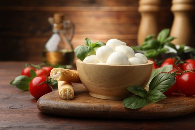Photo of Tasty mozzarella cheese balls, breadsticks, tomatoes and basil on wooden table, closeup