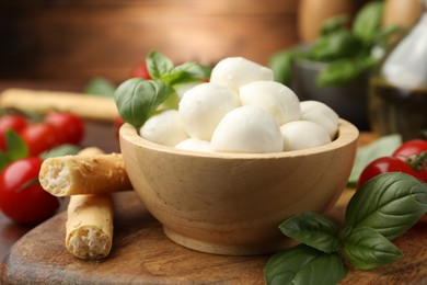 Photo of Tasty mozzarella cheese balls, breadsticks, tomatoes and basil on wooden table, closeup