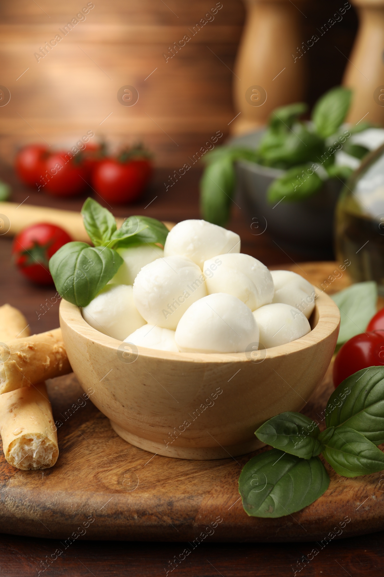 Tasty mozzarella cheese balls, breadsticks, tomatoes and basil on wooden table, closeup Photo of Tasty mozzarella cheese balls, breadsticks, tomatoes and basil on wooden table, closeup