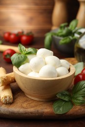 Photo of Tasty mozzarella cheese balls, breadsticks, tomatoes and basil on wooden table, closeup