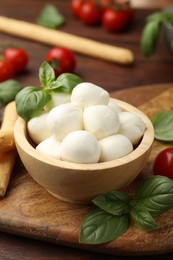 Photo of Tasty mozzarella cheese balls, breadsticks, tomatoes and basil on wooden table, closeup