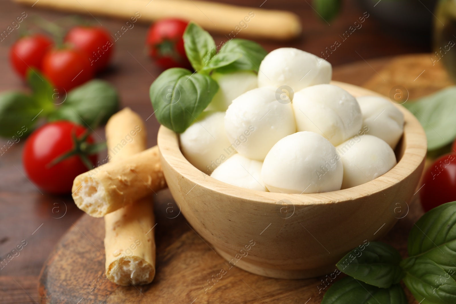 Tasty mozzarella cheese balls, breadsticks, tomatoes and basil on wooden table, closeup Photo of Tasty mozzarella cheese balls, breadsticks, tomatoes and basil on wooden table, closeup