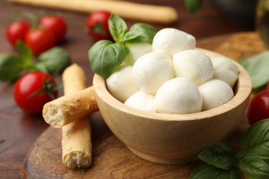 Photo of Tasty mozzarella cheese balls, breadsticks, tomatoes and basil on wooden table, closeup