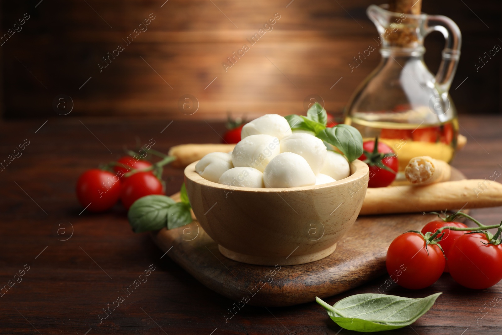 Tasty mozzarella cheese balls, breadsticks, tomatoes and basil on wooden table, closeup Photo of Tasty mozzarella cheese balls, breadsticks, tomatoes and basil on wooden table, closeup