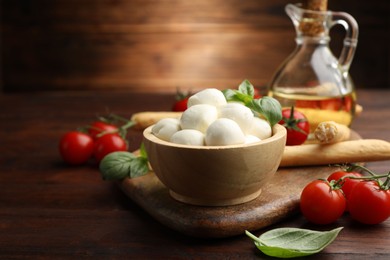 Photo of Tasty mozzarella cheese balls, breadsticks, tomatoes and basil on wooden table, closeup