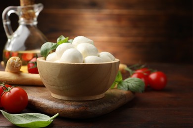 Photo of Tasty mozzarella cheese balls, breadsticks, tomatoes and basil on wooden table, closeup