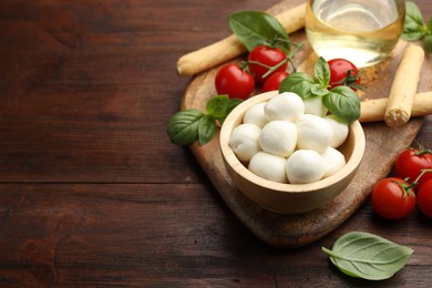 Photo of Tasty mozzarella cheese balls, breadsticks, tomatoes and basil on wooden table. Space for text