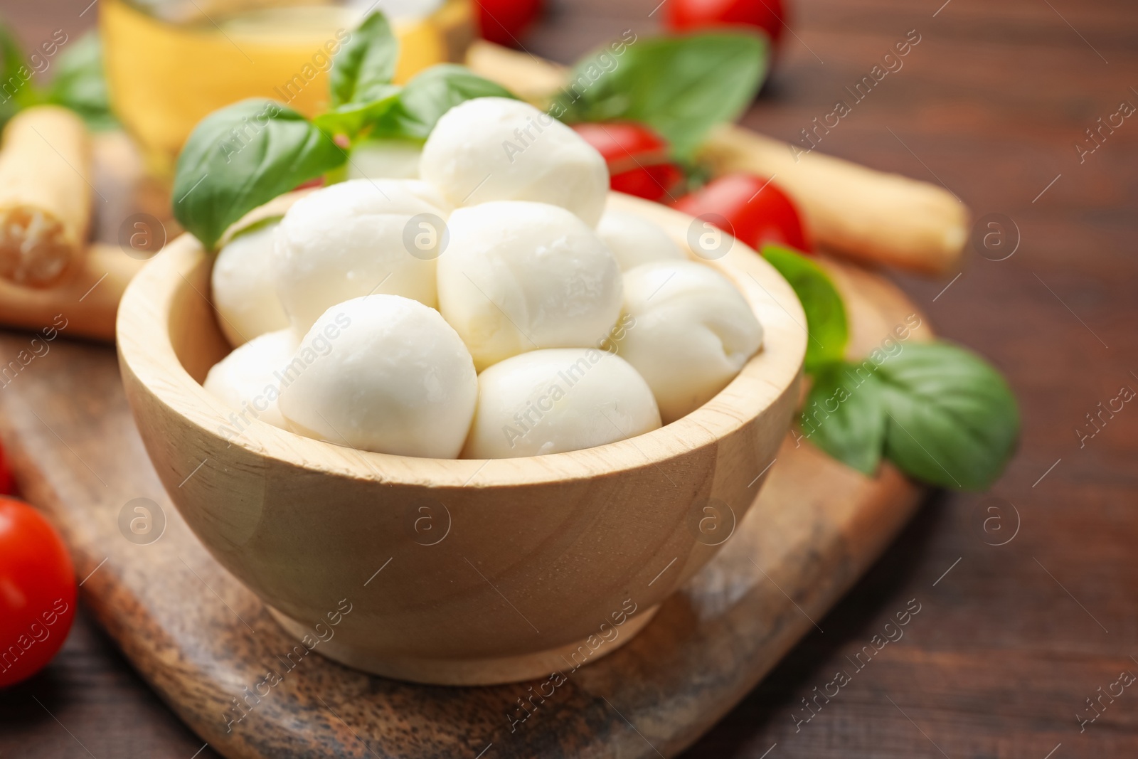 Tasty mozzarella cheese balls, breadsticks, tomatoes and basil on wooden table, closeup Photo of Tasty mozzarella cheese balls, breadsticks, tomatoes and basil on wooden table, closeup