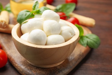Photo of Tasty mozzarella cheese balls, breadsticks, tomatoes and basil on wooden table, closeup