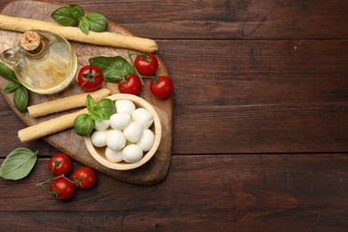Photo of Tasty mozzarella cheese balls, breadsticks, tomatoes and basil on wooden table, flat lay. Space for text