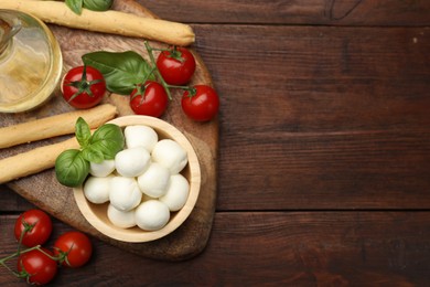 Photo of Tasty mozzarella cheese balls, breadsticks, tomatoes and basil on wooden table, flat lay. Space for text