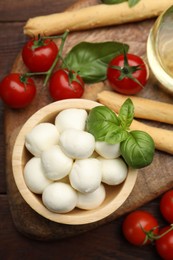 Photo of Tasty mozzarella cheese balls, breadsticks, tomatoes and basil on wooden table, flat lay