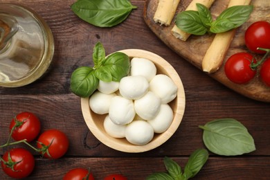 Photo of Tasty mozzarella cheese balls, tomatoes and basil on wooden table, flat lay