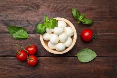 Photo of Tasty mozzarella cheese balls, tomatoes and basil on wooden table, flat lay