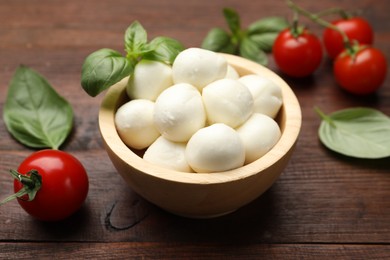 Photo of Tasty mozzarella cheese balls, tomatoes and basil on wooden table, closeup