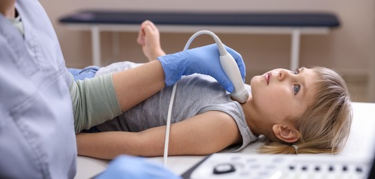 Photo of Sonographer conducting ultrasound examination of little girl's thyroid gland in clinic, closeup