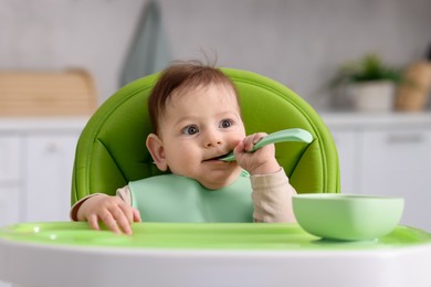 Photo of Cute little baby eating on feeding chair at home
