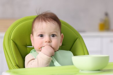 Photo of Cute little baby eating on feeding chair at home. Space for text