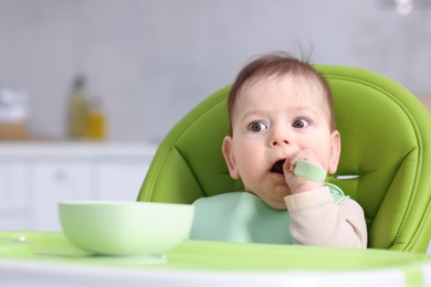 Photo of Cute little baby eating on feeding chair at home. Space for text