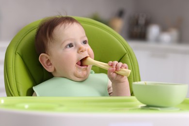 Photo of Cute little baby eating on feeding chair at home