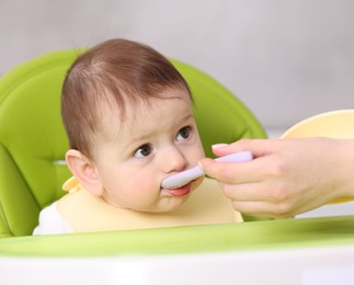 Photo of Mother feeding her baby on chair at home, closeup