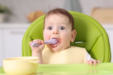 Photo of Cute little baby eating on feeding chair at home