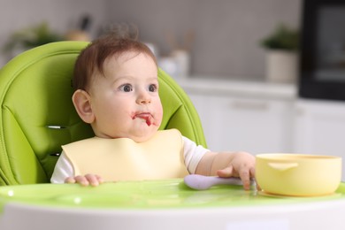 Photo of Cute little baby eating on feeding chair at home