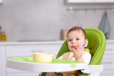 Photo of Cute little baby eating on feeding chair at home. Space for text