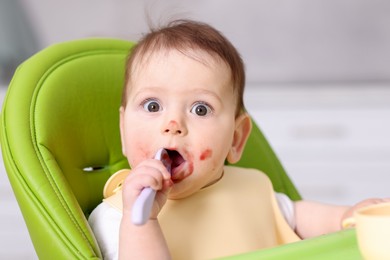 Photo of Cute little baby eating on feeding chair at home