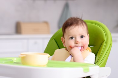 Photo of Cute little baby eating on feeding chair at home. Space for text