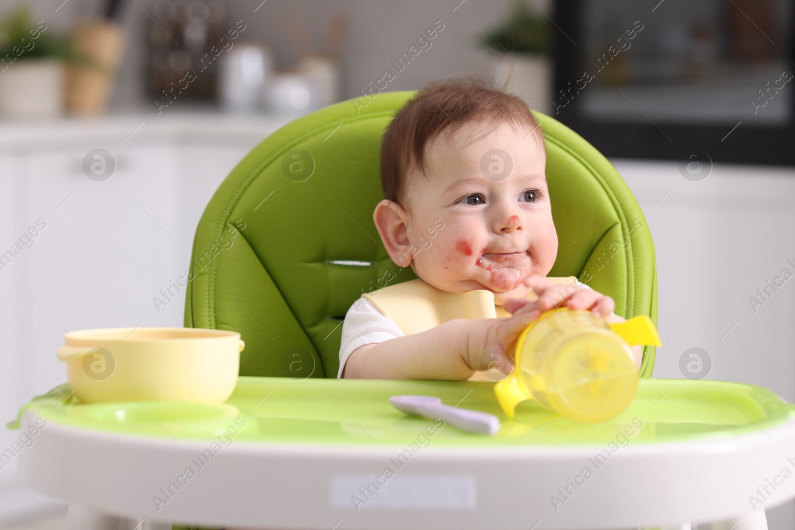 Cute little baby with bottle on feeding chair indoors Photo of Cute little baby with bottle on feeding chair indoors