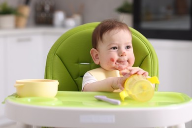 Photo of Cute little baby with bottle on feeding chair indoors